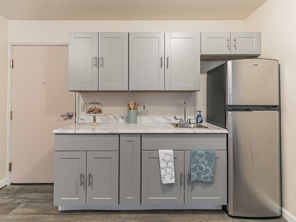 A modern kitchen with gray cabinets and a stainless steel refrigerator.