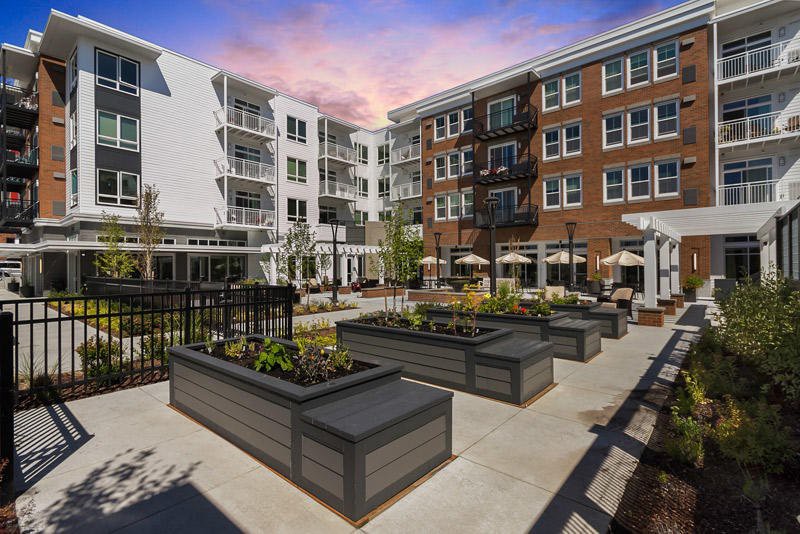 A modern apartment complex with a landscaped courtyard under a colorful evening sky.
