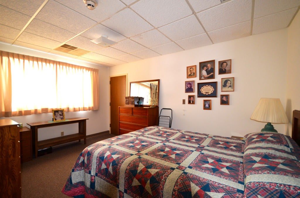 A cozy bedroom with a quilted bedspread and family photos decorating the wall.