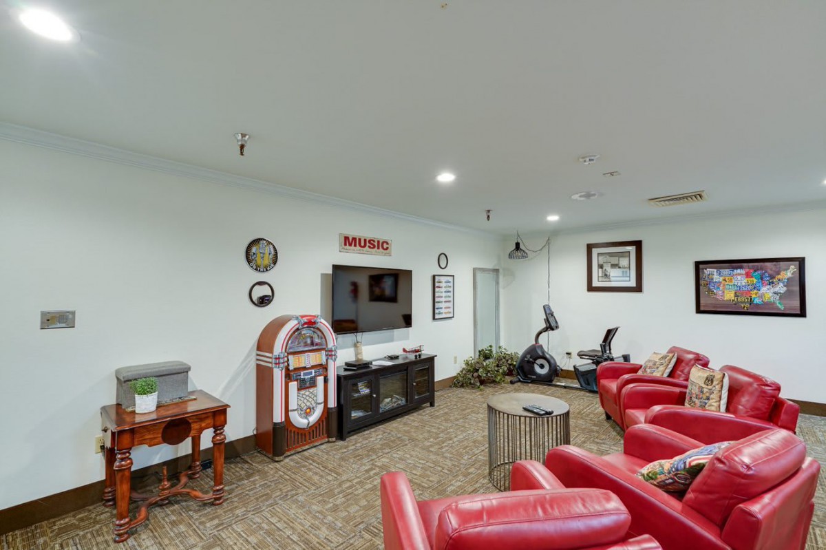 A cozy entertainment room featuring red recliner chairs, a large television, a jukebox, and exercise equipment.