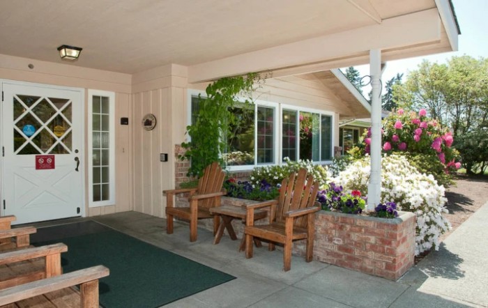 A cozy patio with wooden chairs, surrounded by vibrant plants and flowers.