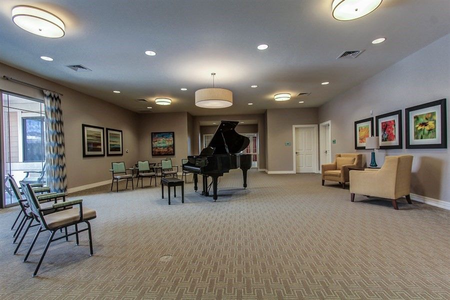 A spacious living room featuring a grand piano and several seating options, adorned with artwork and warm lighting.