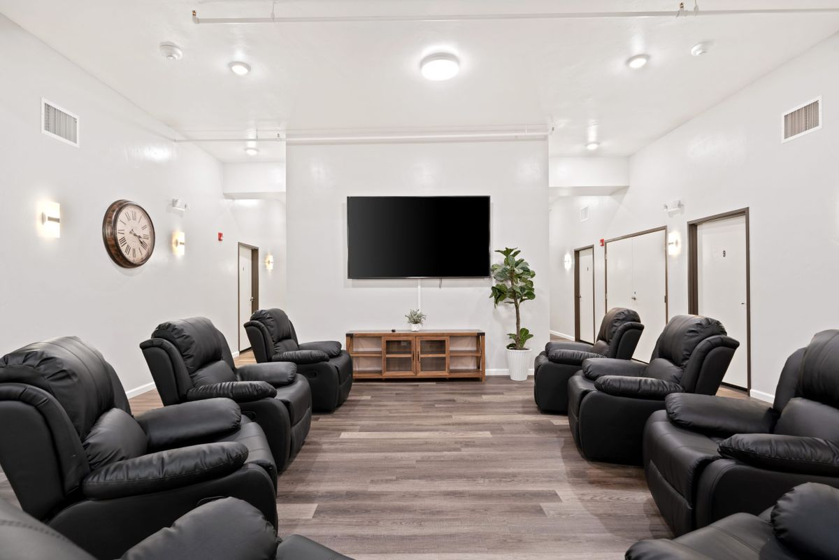 A modern living room with black recliners arranged around a large television on a wooden floor.