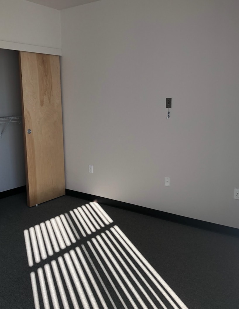 An empty room with sunlight casting shadows through a window, featuring a sliding door and minimalist decor.