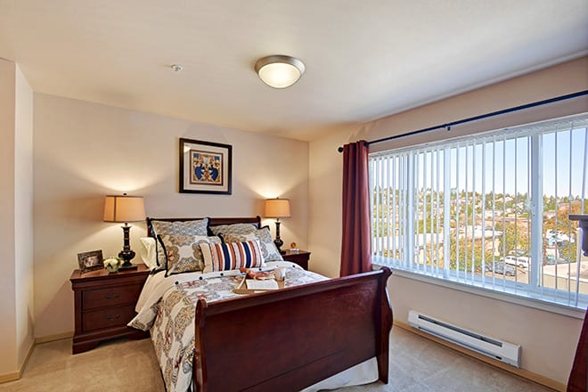A cozy bedroom with a wooden bed, bedside lamps, and a large window.