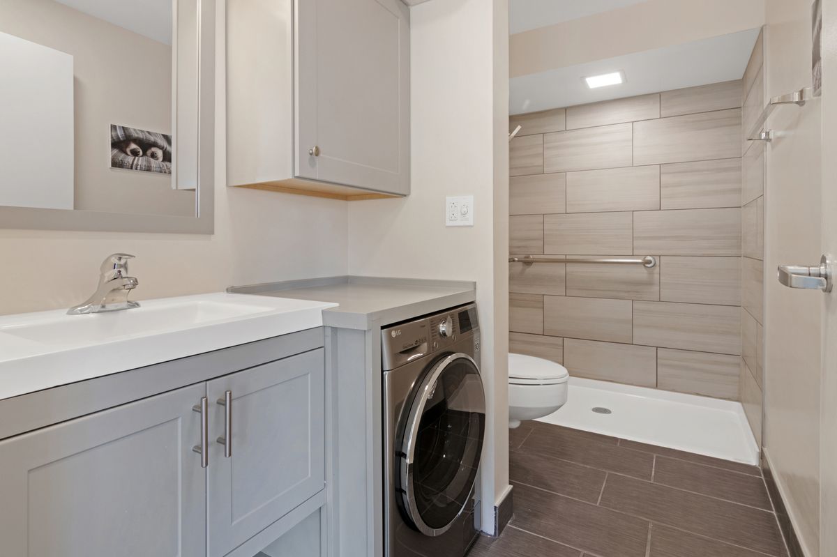 A modern bathroom featuring a washer and dryer alongside a sleek vanity and spacious walk-in shower.