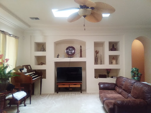 A cozy living room featuring a piano, a TV setup, and decorative shelves.