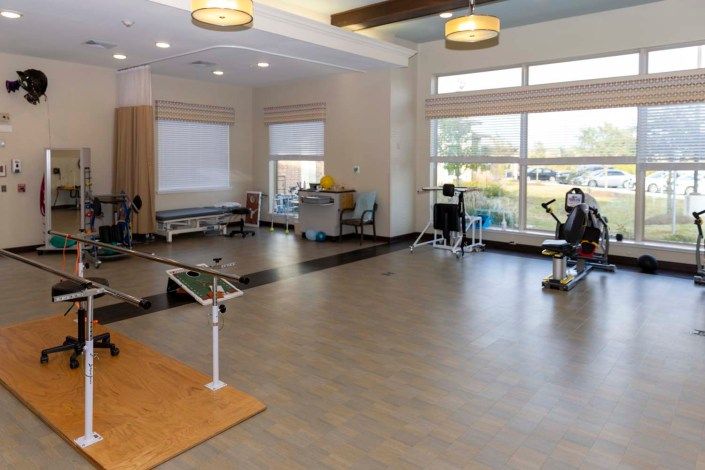 A spacious gym with various exercise equipment and large windows providing natural light.