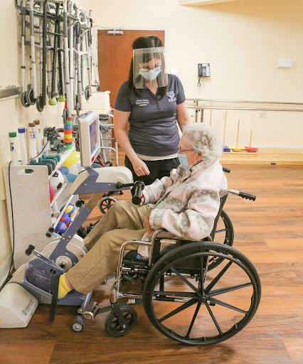 A healthcare worker assists an elderly patient in a wheelchair with medical equipment.