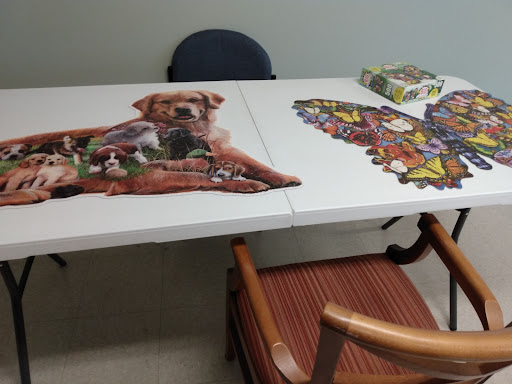 A table with two jigsaw puzzles in progress, featuring a dog and a colorful design.