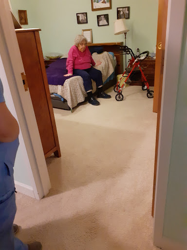 A cozy bedroom scene featuring an elderly person sitting on the bed while a caregiver is in the foreground.
