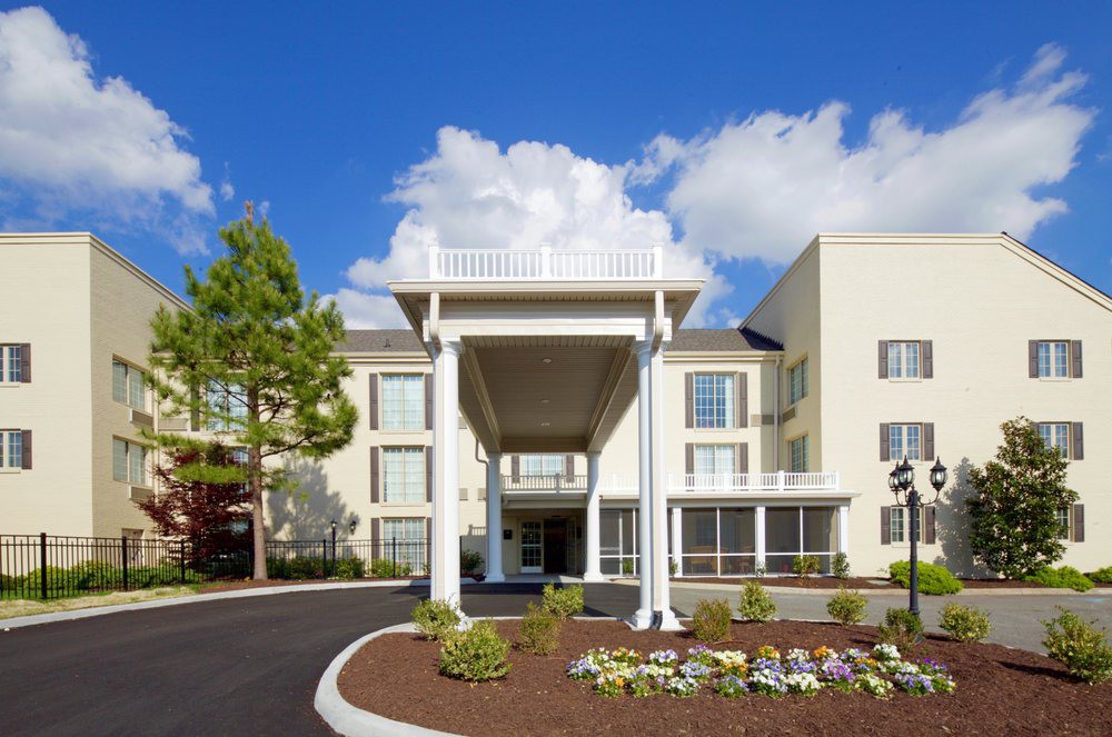 A modern hotel with a grand entrance and well-maintained landscaping under a bright, cloudy sky.