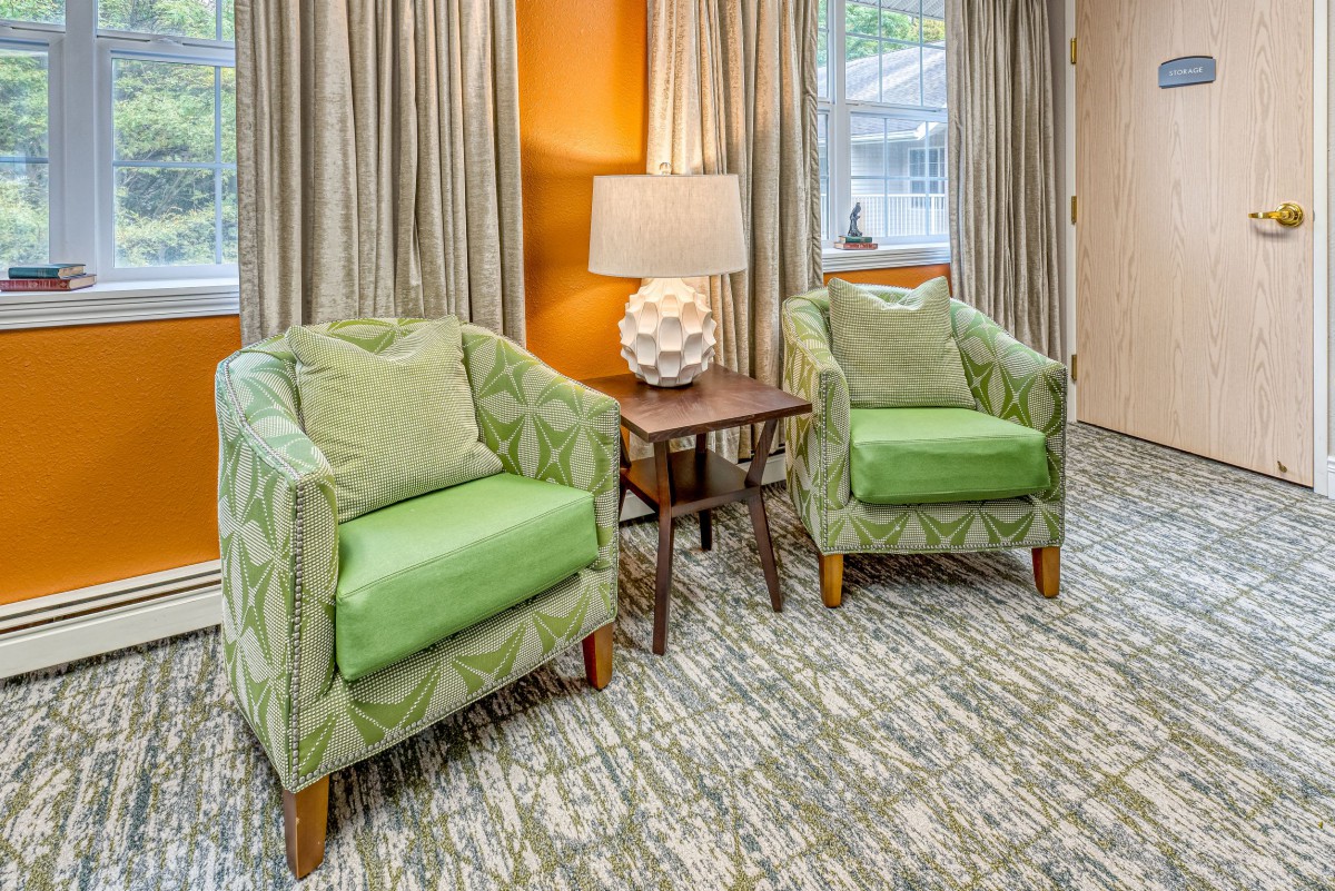 A cozy living room setup featuring two green armchairs, a side table with a decorative lamp, and neutral curtains.