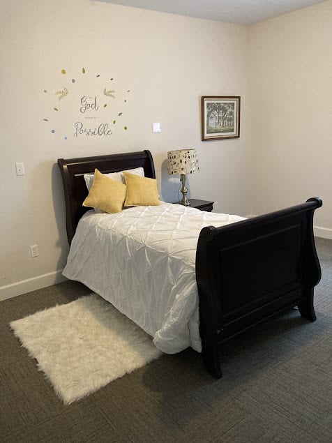 A cozy bedroom featuring a dark wood sleigh bed with white bedding and yellow accent pillows, accompanied by a nightstand and decorative lamp.