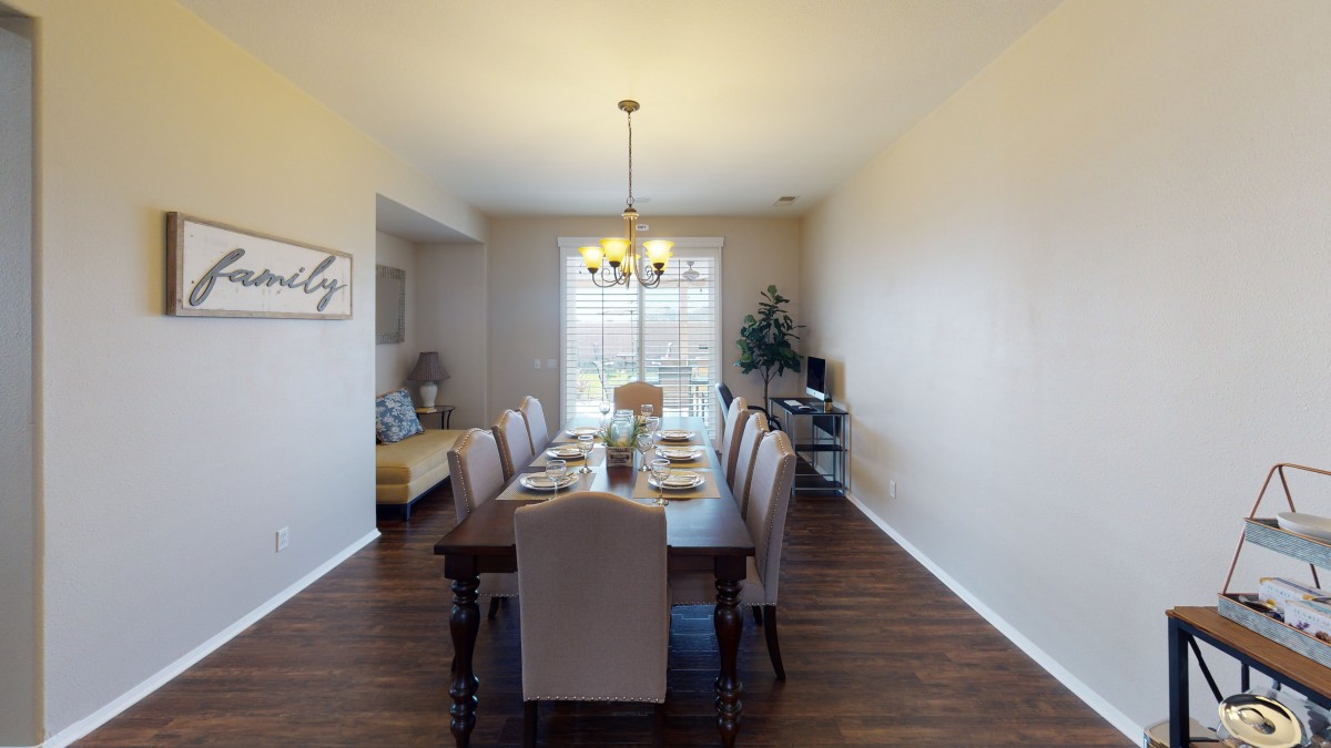 A well-lit dining room with a long table and upholstered chairs, featuring a chandelier and stylish decor.