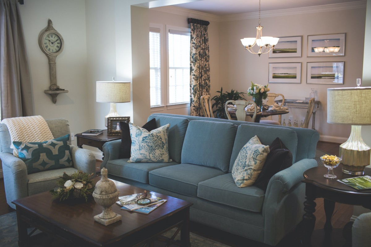 A cozy living room with a blue sofa and a dining area in the background.