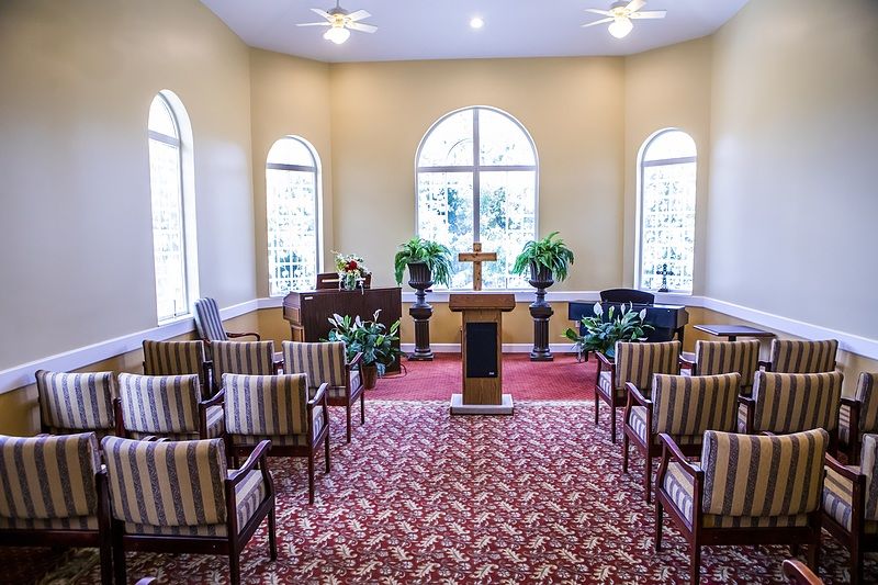 A view of a small chapel interior with striped chairs, podium, and decorative plants.