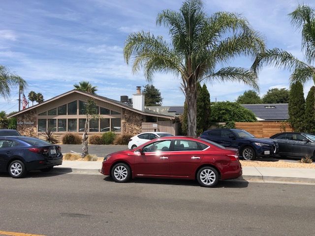 A suburban street with a red car parked in front of a house with a palm tree.