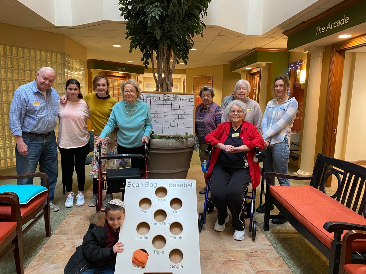 A group of people, including elderly individuals and a child, gather indoors for a fun game.