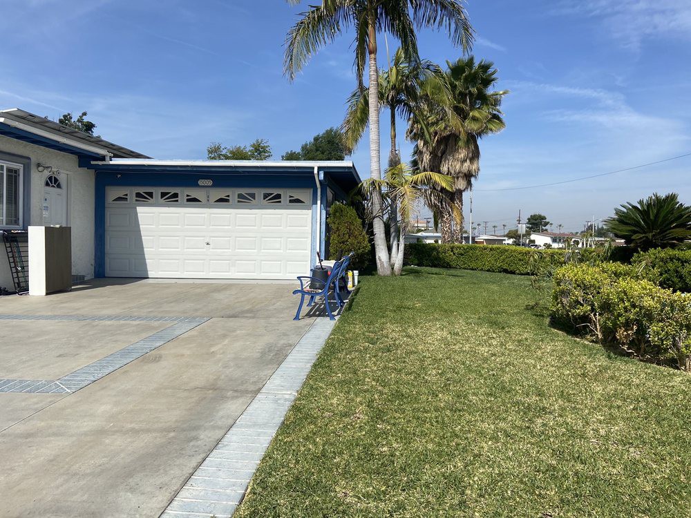 A suburban house with a garage and well-maintained lawn, featuring palm trees.