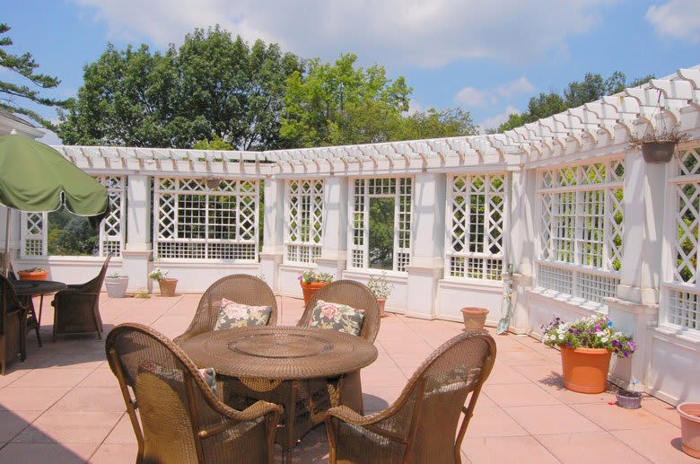 A sunny patio with wicker chairs and a table under a white lattice pergola.