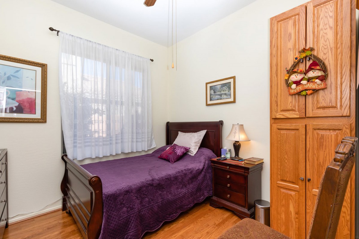 A cozy bedroom with a wooden bed, nightstand, lamp, and a window with sheer curtains.