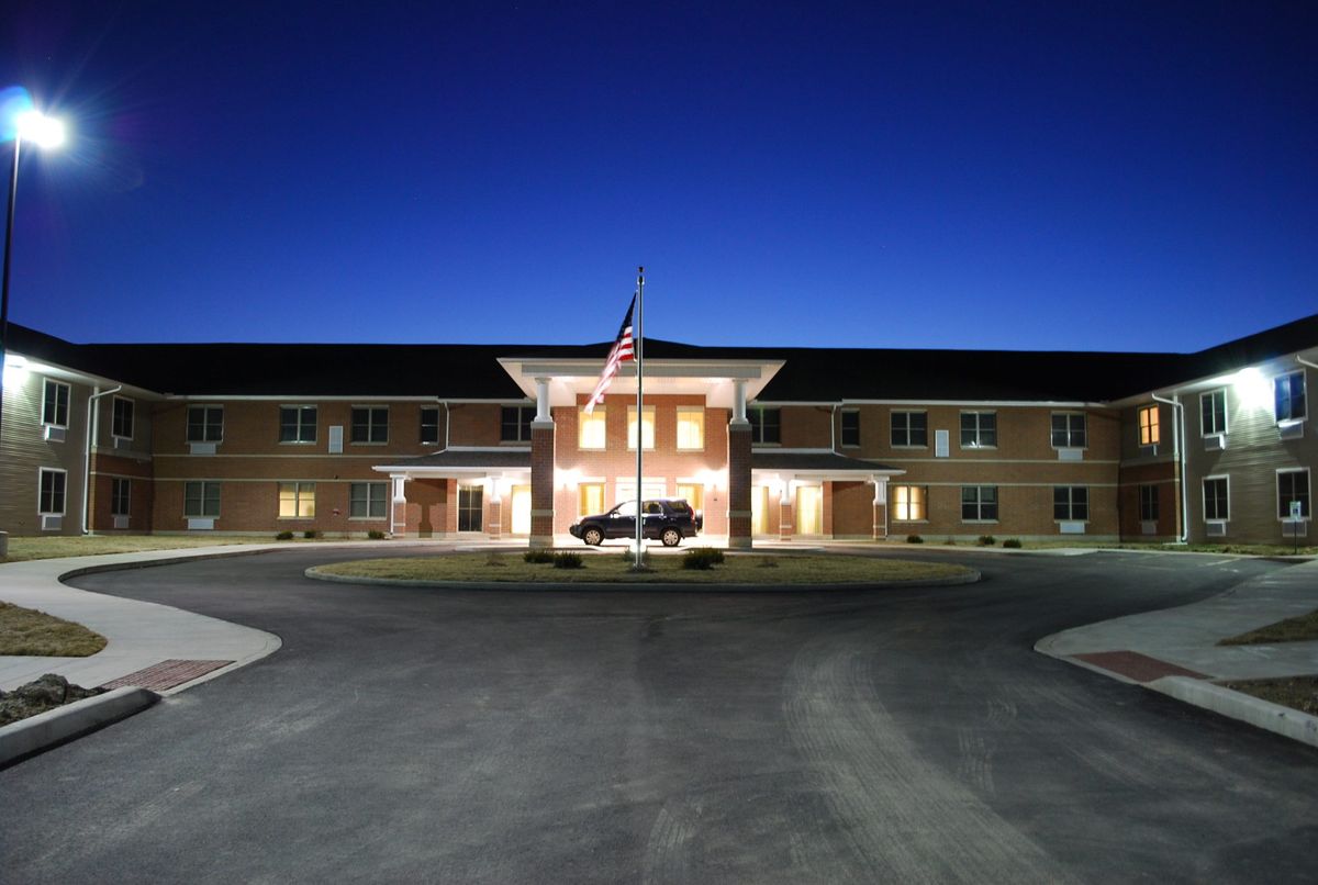 A well-lit building entrance at night with a flag in front.