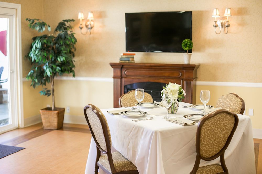 A neatly set dining table in a cozy room with a fireplace and television.