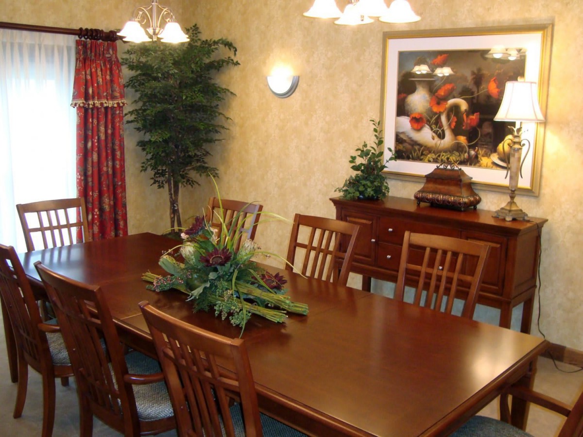 A beautifully decorated dining room with a long wooden table and chairs, complemented by plants and artwork.