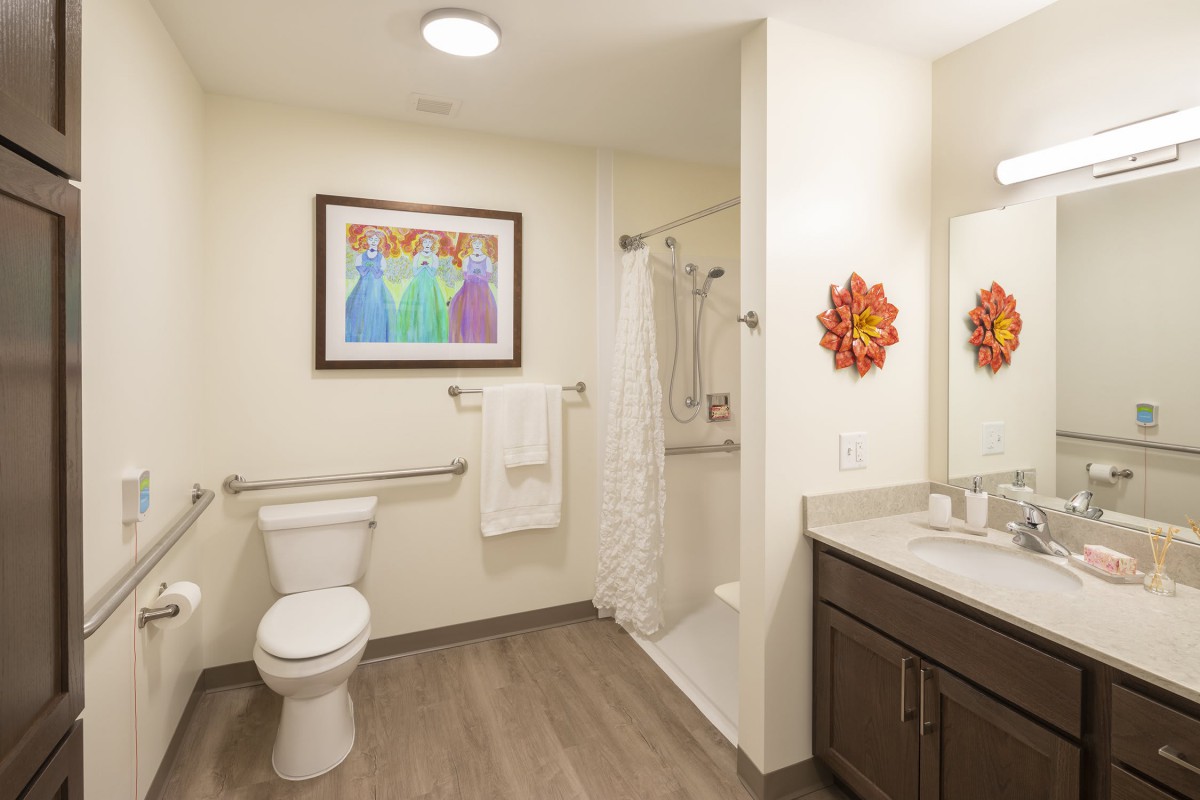 A modern bathroom featuring a toilet, shower, and vanity with decorative artwork on the walls.