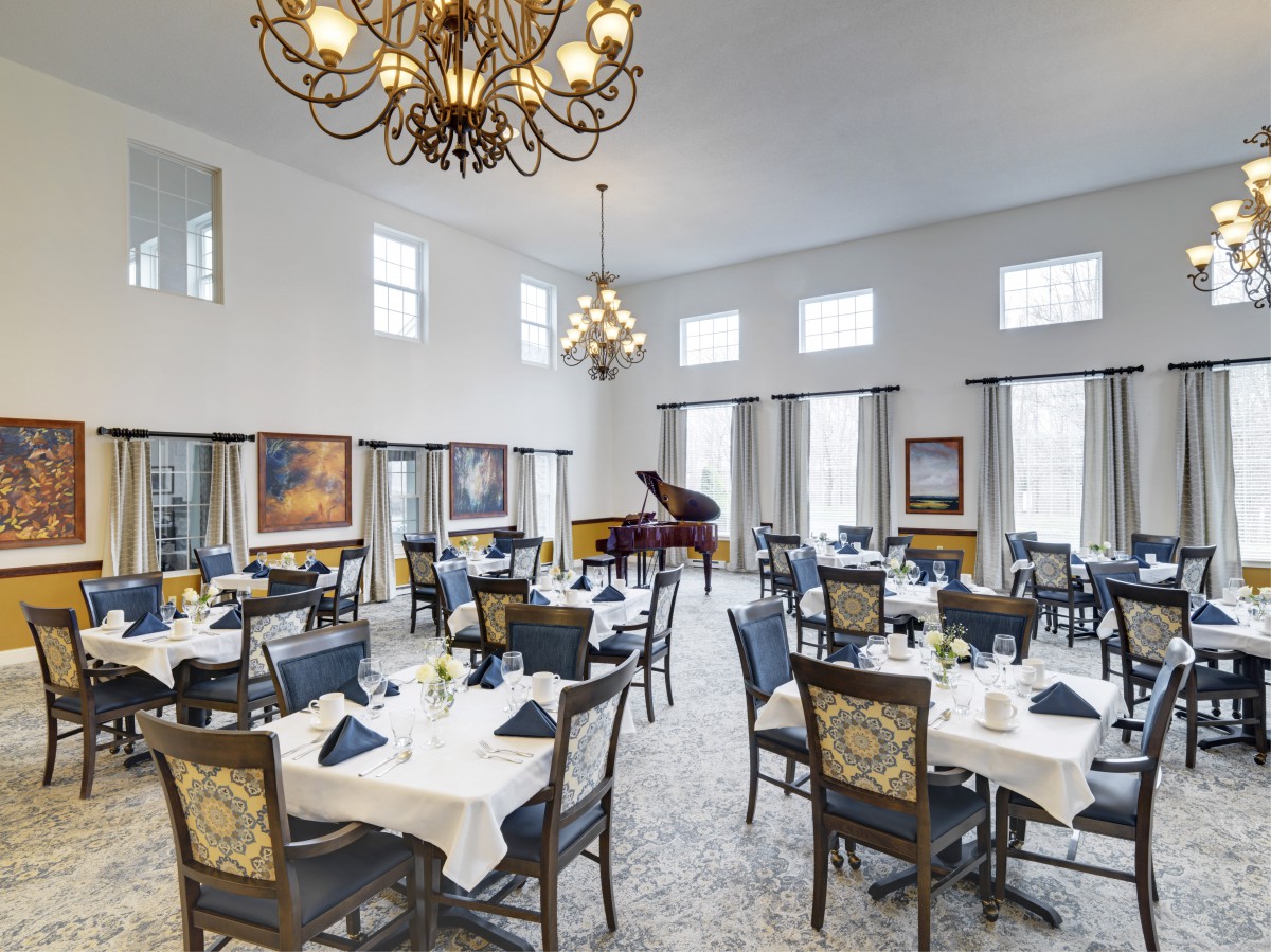 A spacious and elegant dining room featuring white tablecloths, a grand piano, and ornate chandeliers.