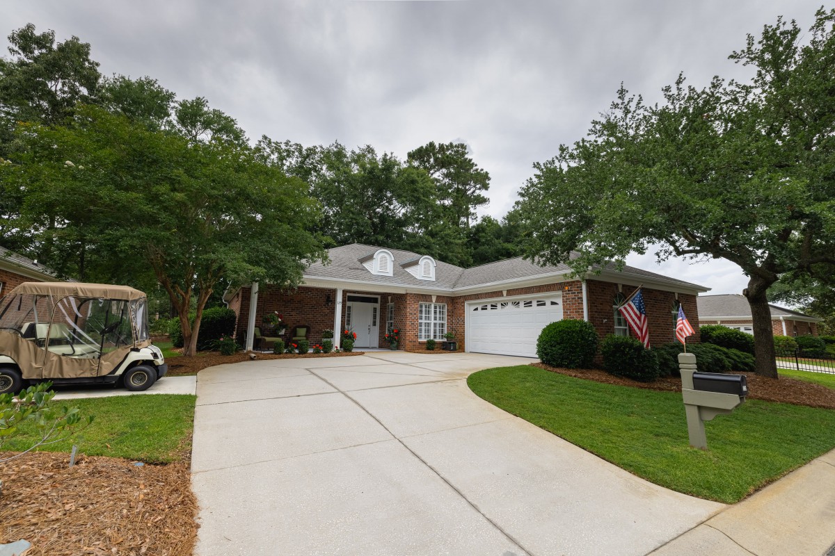 A suburban house with a neatly maintained lawn and driveway, displaying American flags on a cloudy day.