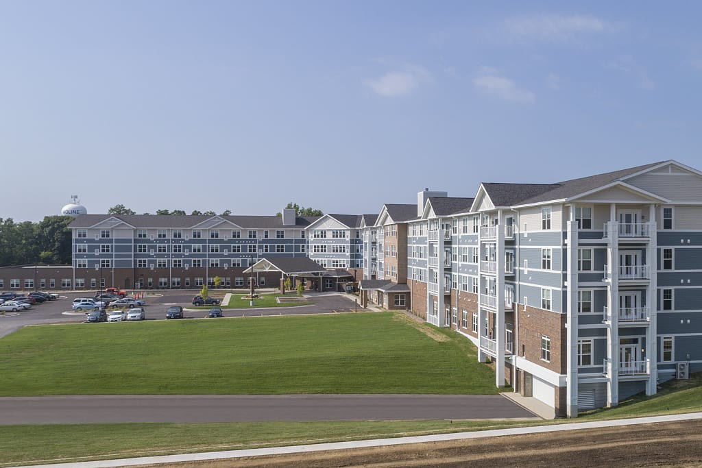 A suburban residential apartment complex with expansive grassy areas under a clear blue sky.