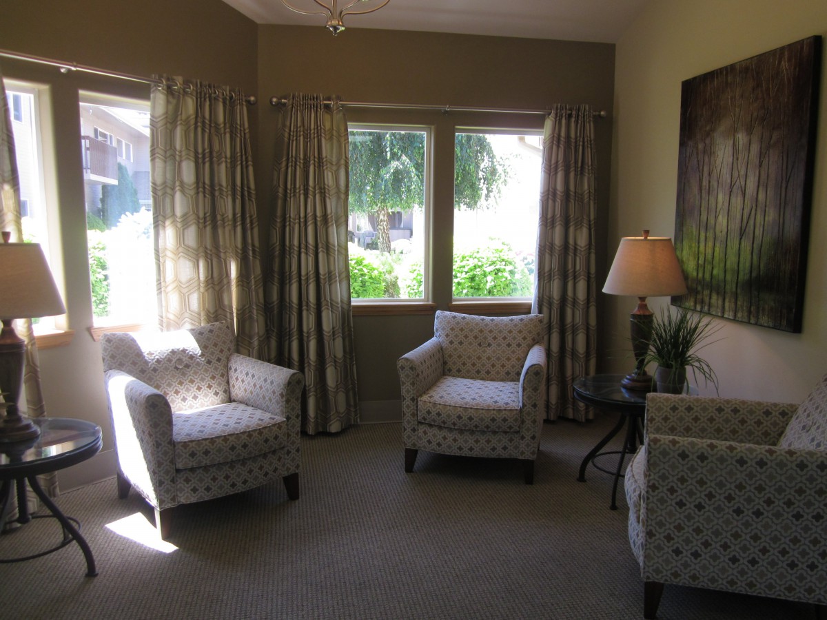 A cozy living room with armchairs, a small table, and a lamp by the window allowing natural light.