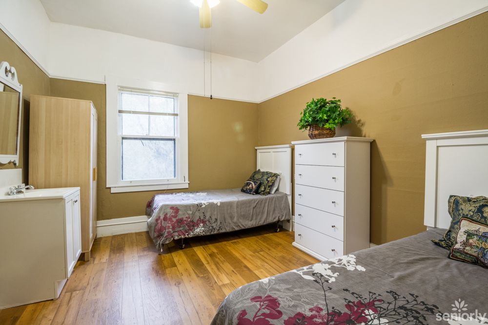 A cozy bedroom featuring twin beds with floral bedding, a dresser with a potted plant, and hardwood flooring.