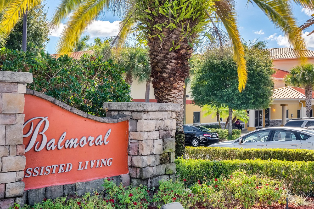 A scenic view of an assisted living facility with a prominent sign and surrounding palm trees.