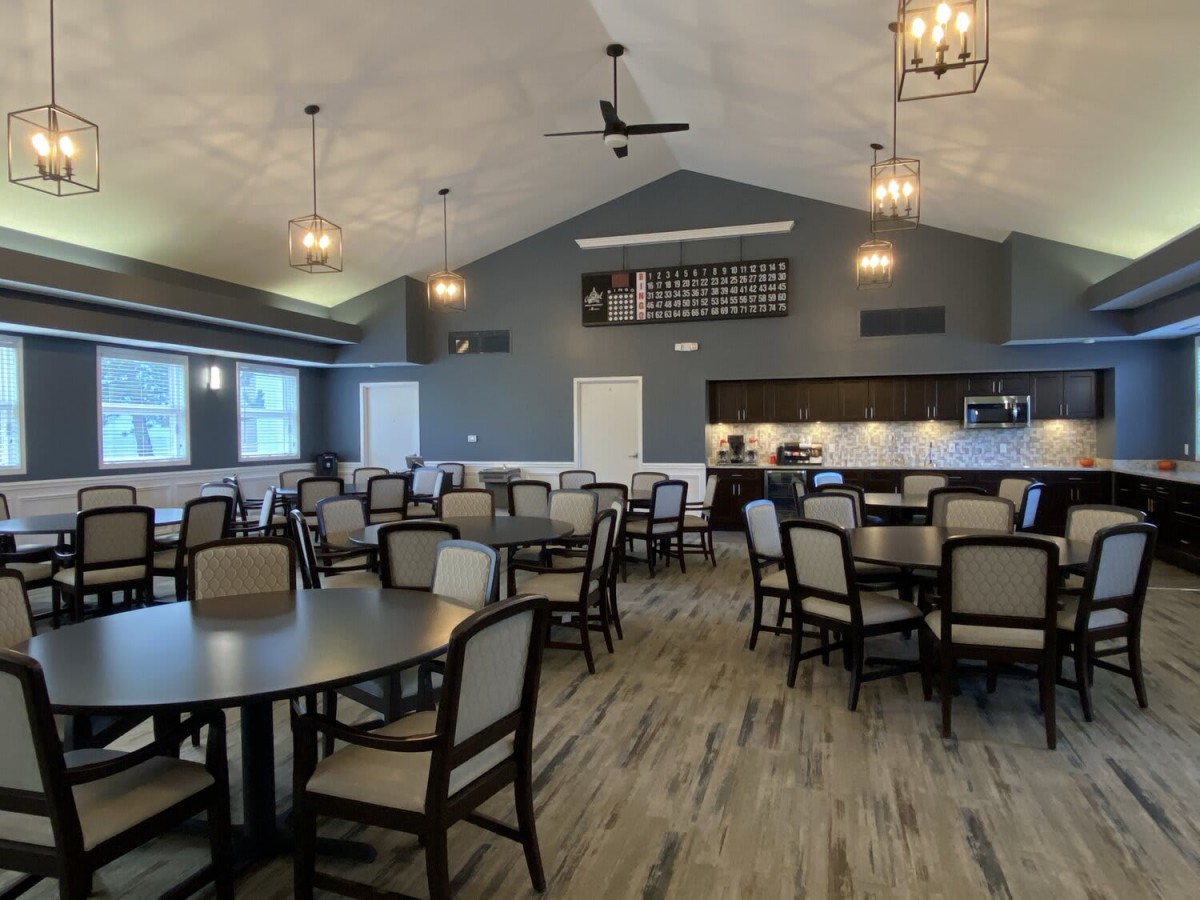 A spacious dining area with tables and chairs, featuring a kitchen area and stylish lighting.