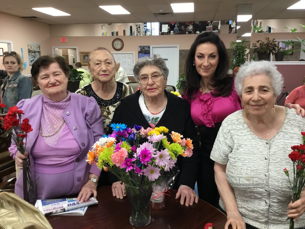 A group of women posing together indoors with a colorful bouquet of flowers on the table.