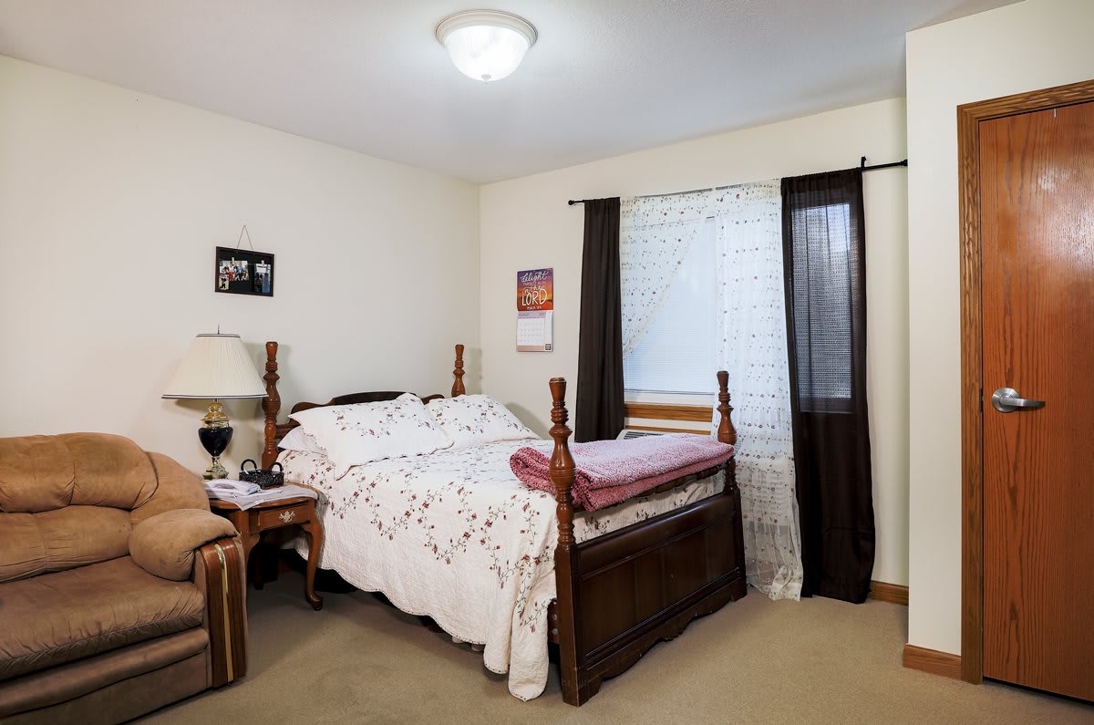 A cozy bedroom with a wooden bed, nightstand, and window with curtains.