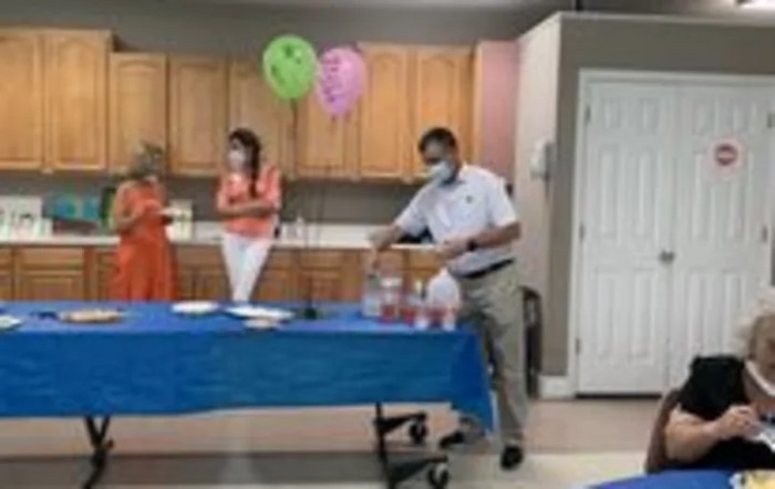 A group of people wearing masks gathered around a table with balloons overhead.