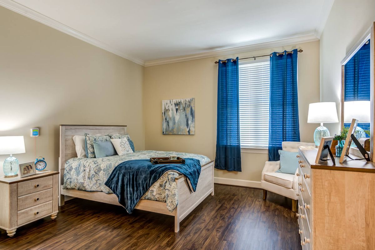 A modern bedroom featuring a bed with blue-themed bedding, complemented by matching curtains and a cozy armchair, all set on elegant wood flooring.
