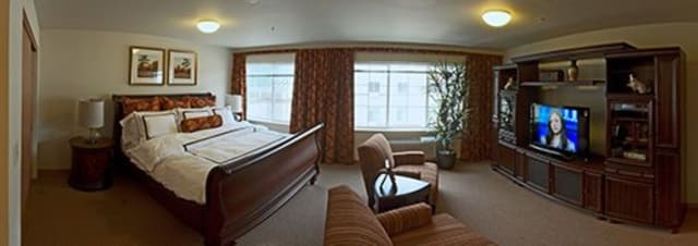 A cozy hotel room featuring a large bed, two chairs, and natural light streaming through the windows.