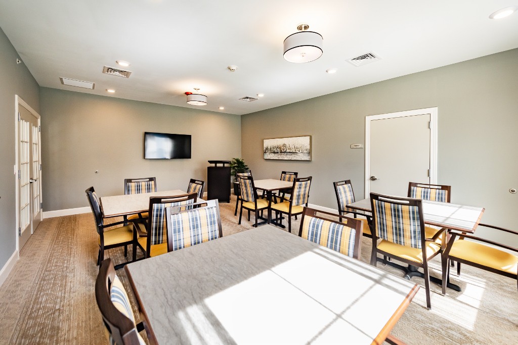A modern meeting room with several tables and chairs, featuring a television on the wall and bright lighting.
