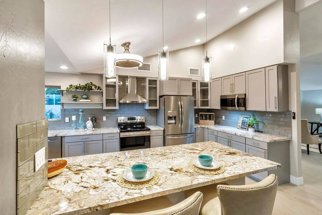 A modern kitchen with stainless steel appliances, a large granite island, and pendant lighting.