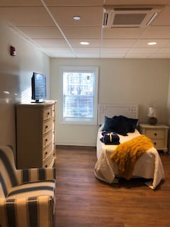 A cozy bedroom with a single bed, television, and a window letting in natural light.
