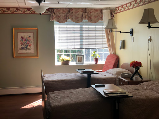 A cozy patient room featuring two beds, natural light pouring in from the window, and decorative touches for a comforting atmosphere.