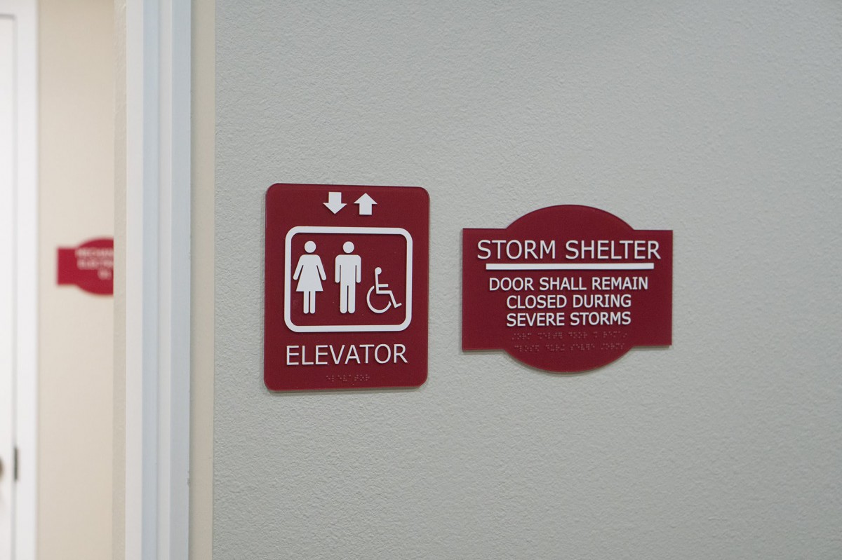 A pair of signs indicating the locations of an elevator and a storm shelter, emphasizing accessibility features and safety instructions.