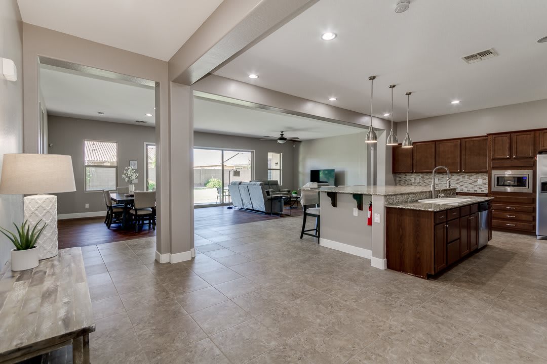 A modern open-concept living space featuring a kitchen, dining area, and living room with tile flooring and pendant lighting.