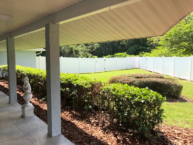 A view of a well-maintained yard with a white fence and neatly trimmed bushes from the patio.