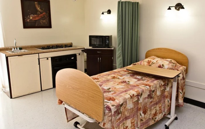 A hospital room featuring a bed with a floral-patterned cover, medical equipment, and simple furnishings.